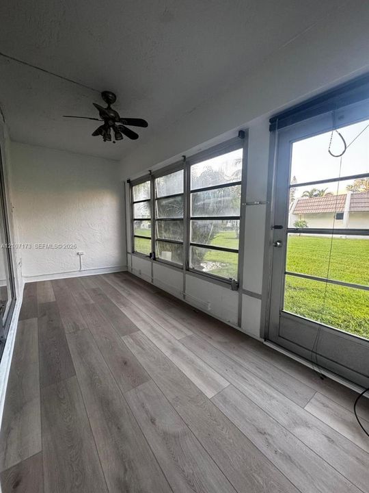 Enclosed porch featuring wood-finish flooring, white textured walls, multi-panel windows, and a ceiling-mounted fan