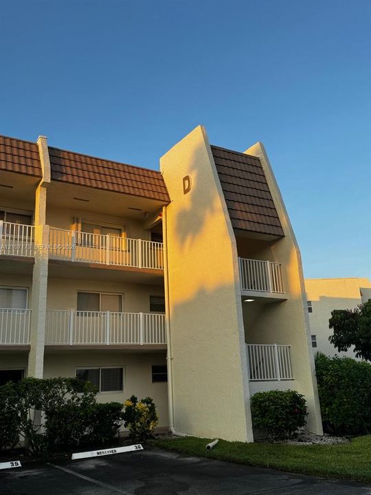 Multi-story stucco exterior featuring a brown tiled mansard roof, white metal railings, and integrated balconies