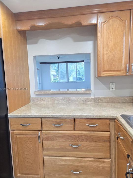 Kitchen featuring stained wood cabinetry, stone-finish countertops, integrated matching backsplash, and a pass-through window with a stone-finish sill