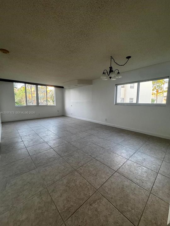 Large open space featuring neutral tile flooring, multiple windows, and a classic multi-light chandelier