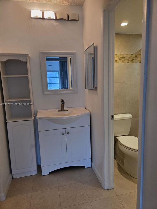Bathroom featuring a vanity with an integrated sink, polished metal faucet, built-in shelving unit, wall-mounted mirror, and tile flooring
