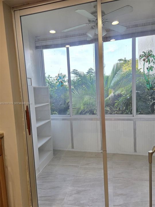 Enclosed sunroom featuring large-pane windows, stone-tile flooring, built-in shelving, a ceiling fan, and recessed lighting