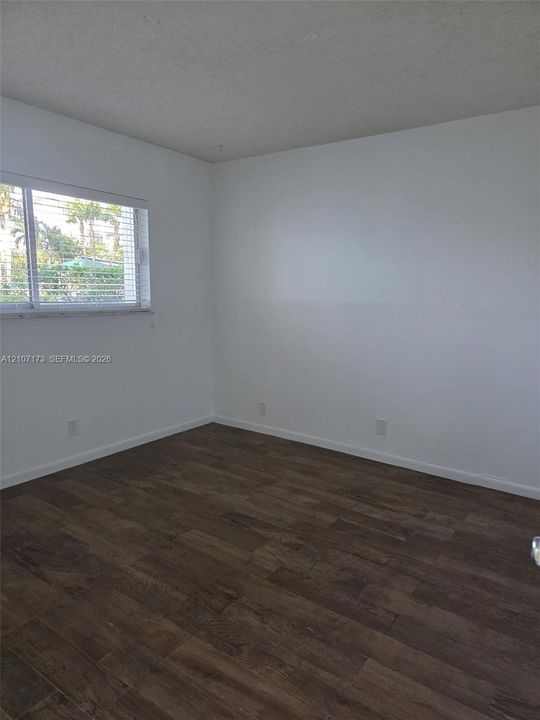 Interior space featuring wood-finish flooring, white walls, and a window with horizontal blinds