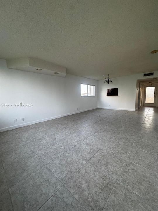 Open-concept area featuring oversized neutral floor tile, recessed soffit lighting, and a multi-arm decorative ceiling fixture