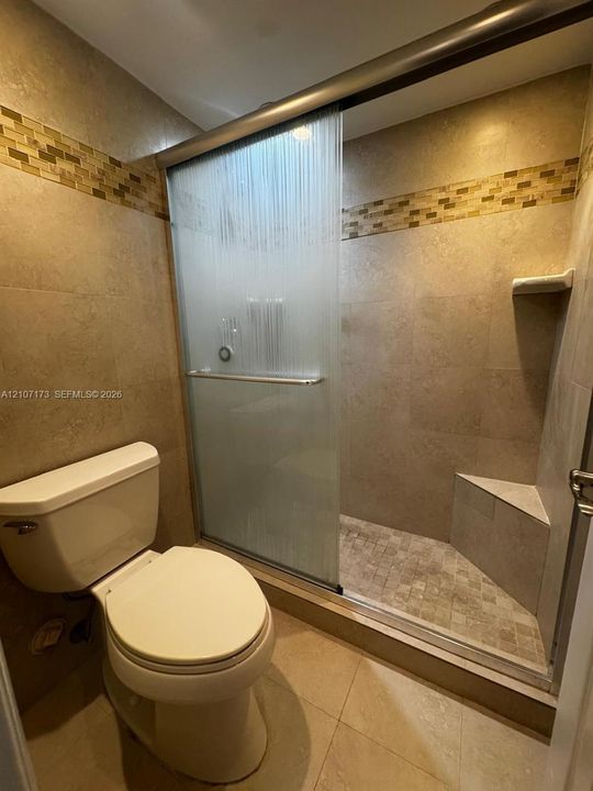 Walk-in shower featuring a textured sliding glass door, built-in corner bench, and neutral wall tiling with a mosaic accent border