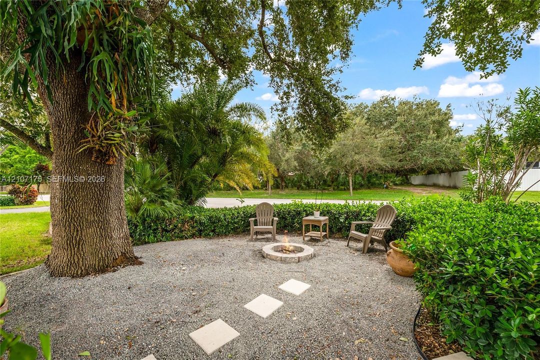 Outdoor space featuring a gravel courtyard, a circular stone fire pit, paver stones, and mature landscape elements.