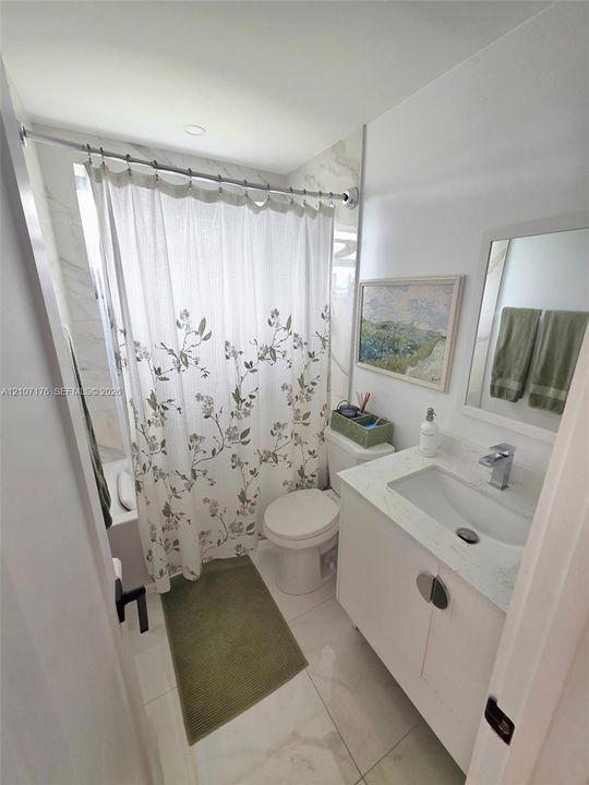 Bathroom featuring a vanity with a white composite countertop, an undermount sink, a chrome faucet, large-format tile flooring, and a tub-shower enclosure with tiled surround