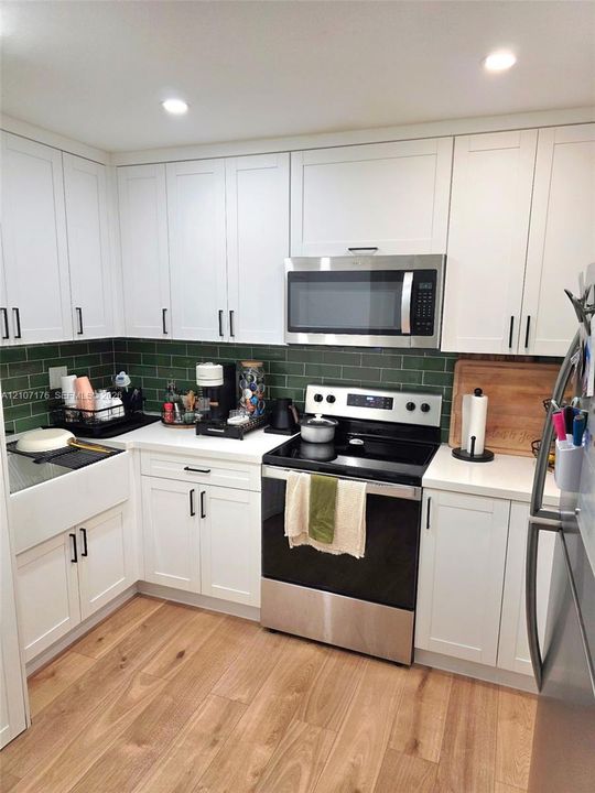 Kitchen featuring white shaker-style cabinetry, green subway tile backsplash, white countertops, farmhouse-style sink, and wood-finish flooring