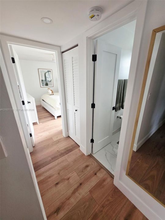 Hallway featuring wood-finish flooring, white louvered closet doors, and solid-core interior doors with matte black hardware