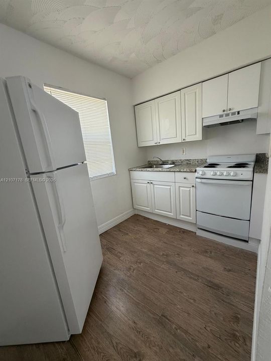 Kitchen featuring white cabinetry, stone-finish countertops, wood-finish flooring, and built-in white appliances