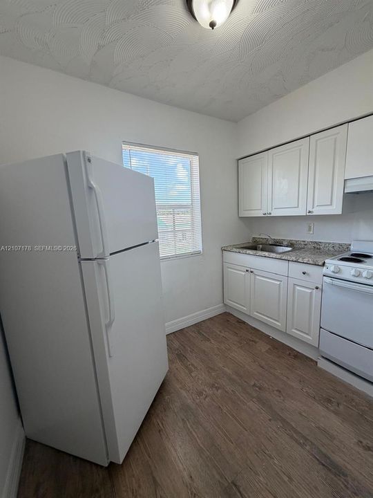 Kitchen featuring white cabinetry, stone-finish countertops, wood-finish flooring, and a single-basin stainless steel sink