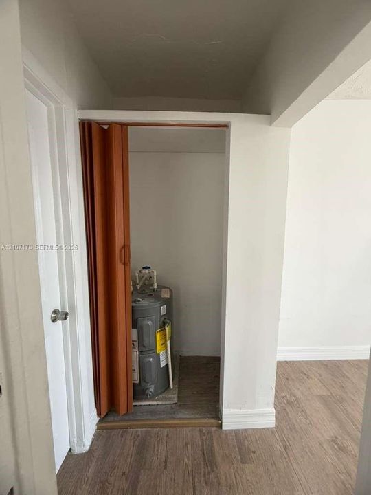 Utility closet featuring an accordion-style folding door and wood-finish flooring