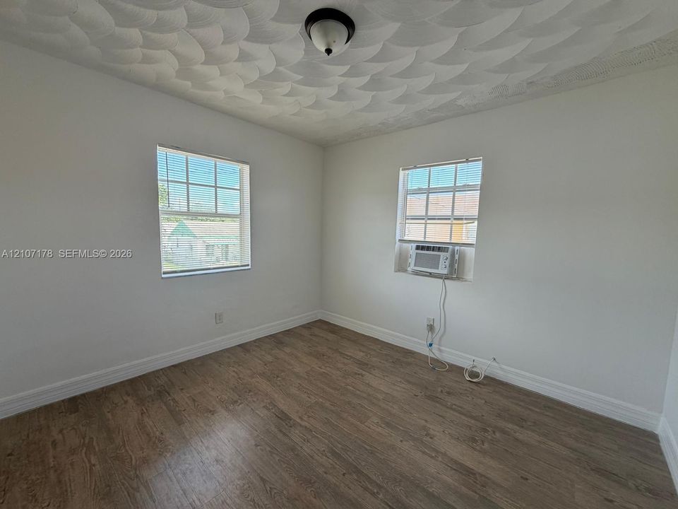 Room featuring wood-finish flooring, textured ceiling, dual windows with grid detailing, and wall-mounted air conditioning unit