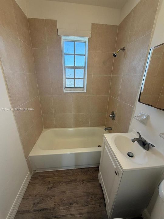 Bathroom featuring a tub-shower combination with floor-to-ceiling tile surround, a single-basin vanity with cabinet storage, and wood-finish flooring