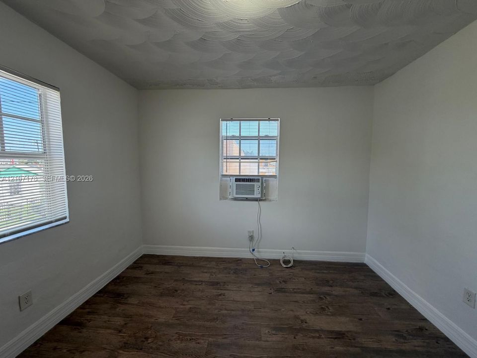 Room featuring wood-finish flooring, textured ceiling, dual windows with grid-patterned glass, and an integrated window-mounted air conditioning unit