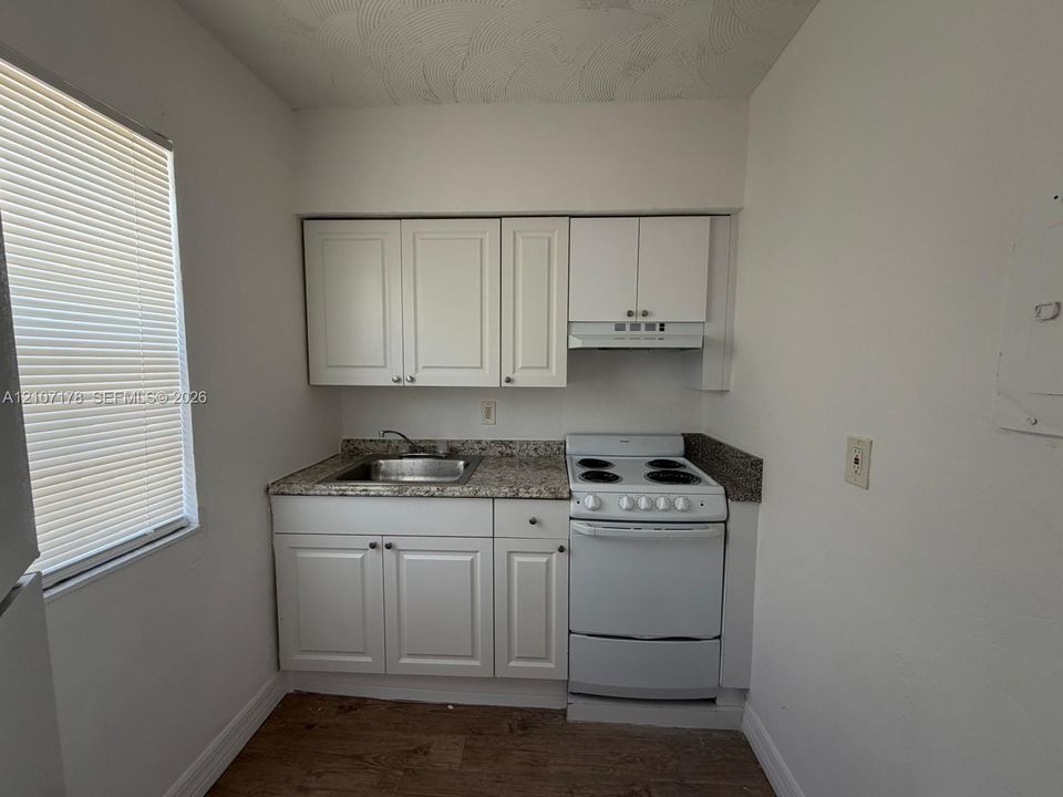 Kitchen area featuring white shaker-style cabinetry, stone-finish countertops, stainless steel sink with a mounted faucet, integrated white electric range, and wood-finish flooring
