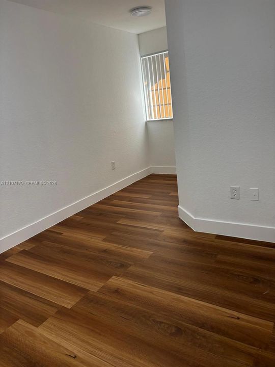 Interior space featuring wood-finish flooring, white walls, and a recessed window with vertical blinds