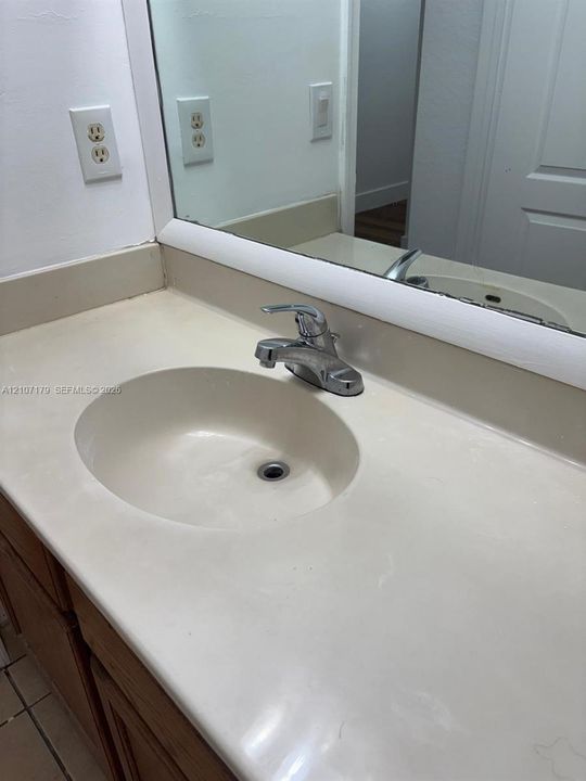 Integrated vanity featuring a solid-surface countertop with an inset basin, a single-handle chrome faucet, and a large-format mirror with a white trim frame