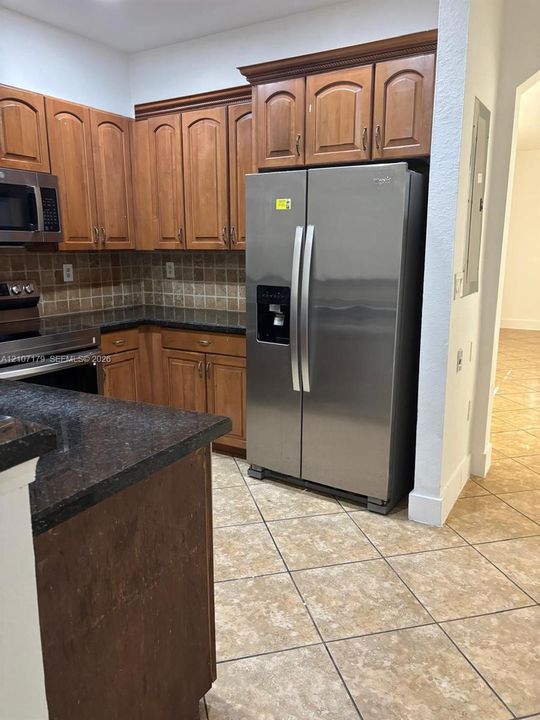 Kitchen featuring wood cabinetry, stone-finish countertops, stainless steel appliances, a tiled backsplash, and ceramic tile flooring