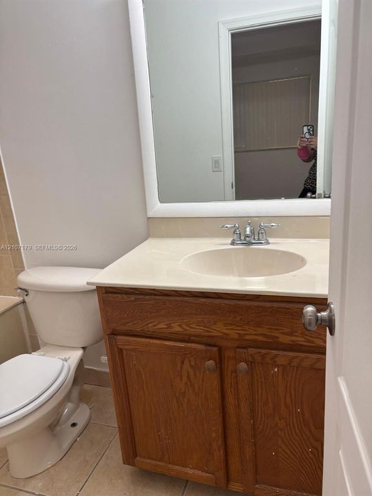 Wood-finish vanity cabinet featuring an integrated sink, solid surface countertop, chrome dual-handle faucet, and a large wall-mounted mirror