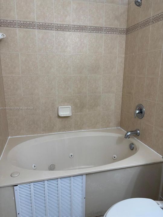 Jetted soaking tub with a tiled surround, built-in recessed soap dish, decorative tile inlay, and chrome finish faucet hardware