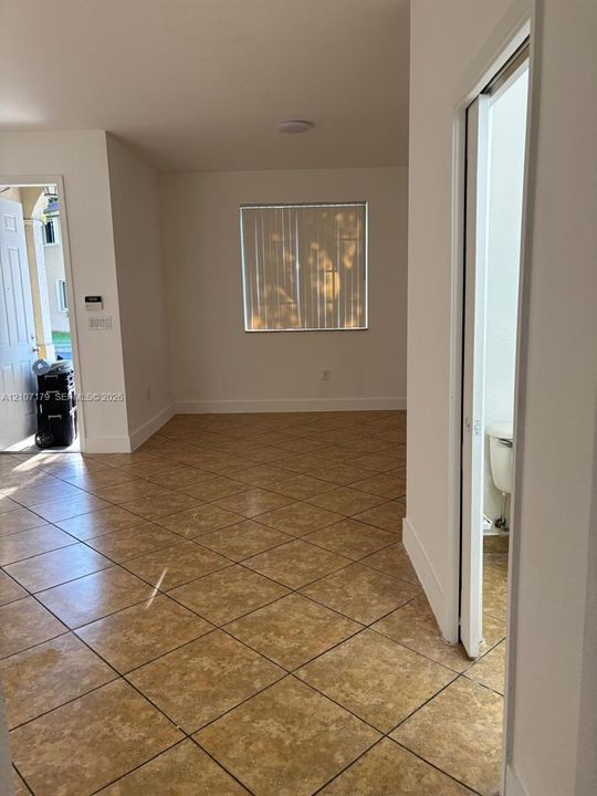 Neutral-toned ceramic tile flooring laid on a diagonal, crisp white interior wall finish, and a window with vertical blinds