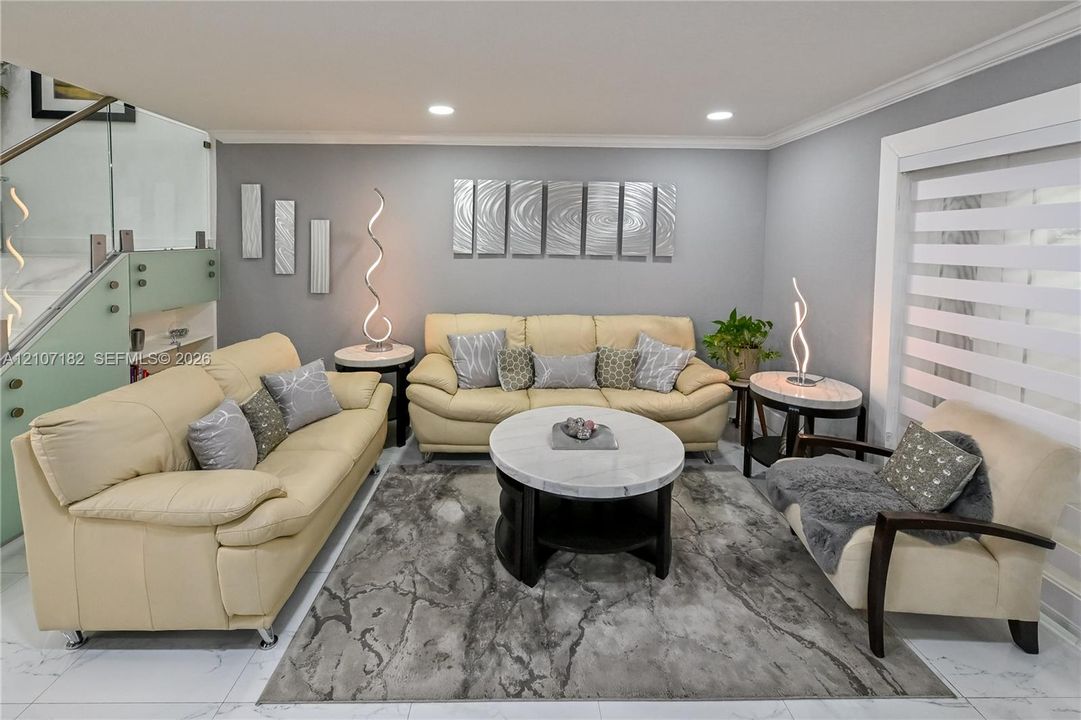 Living area featuring polished tile flooring, recessed lighting, and a staircase with glass panel railing