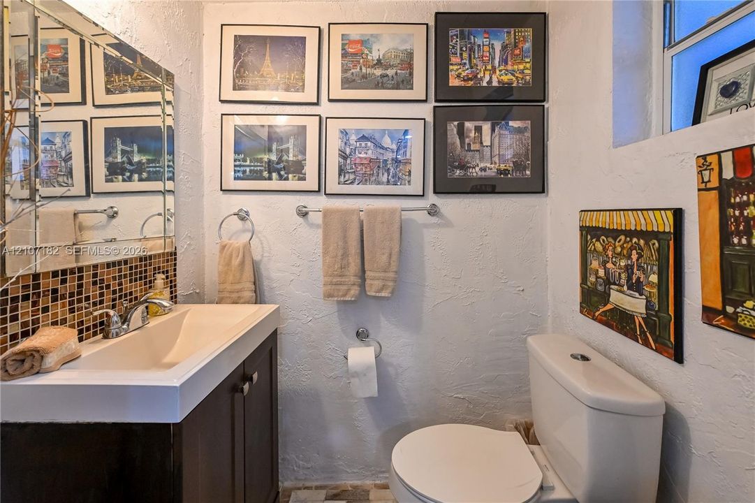 Bathroom featuring a dark-finish vanity with a rectangular integrated sink, chrome-finish faucet, multi-colored square mosaic tile backsplash, and large wall-mounted mirror
