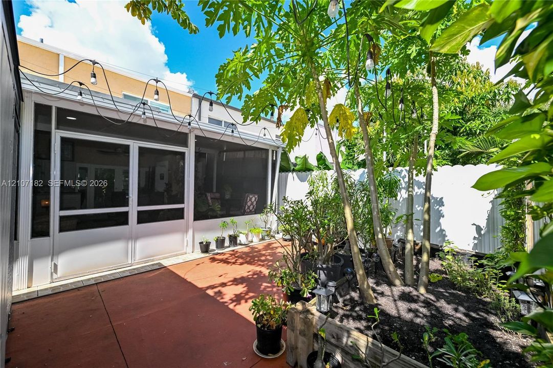 Screened-in patio with hardscaped flooring, white perimeter fencing, and integrated overhead string lighting