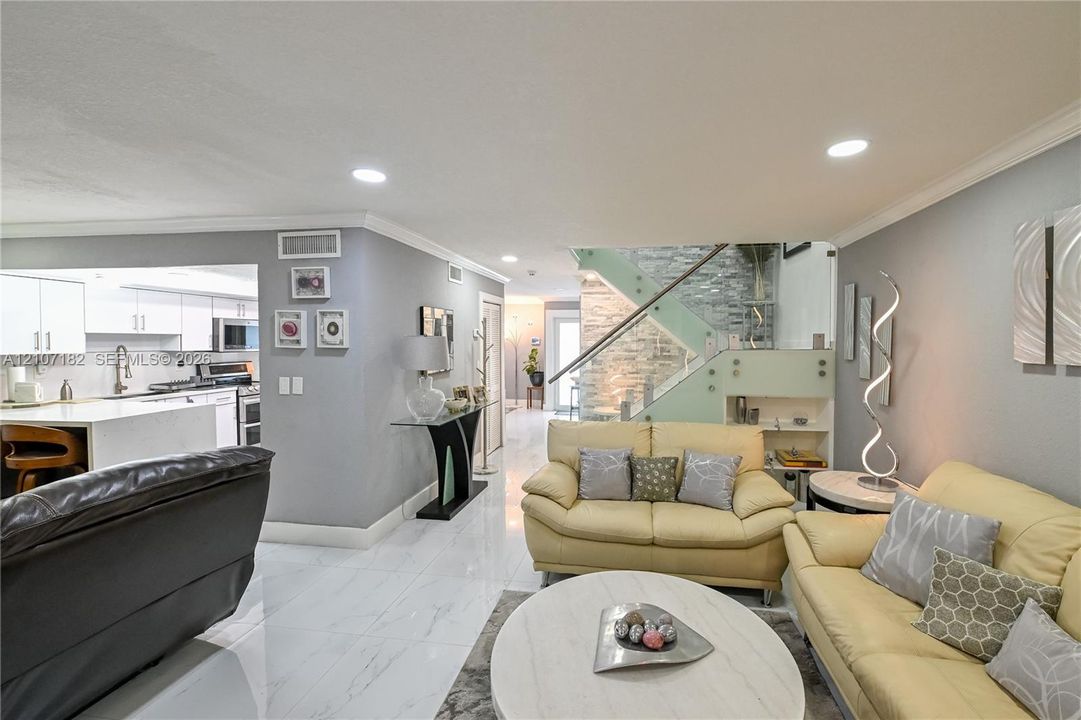 Interior featuring large-format tile flooring, recessed lighting, and a staircase with glass panel railing and stone-textured accent wall