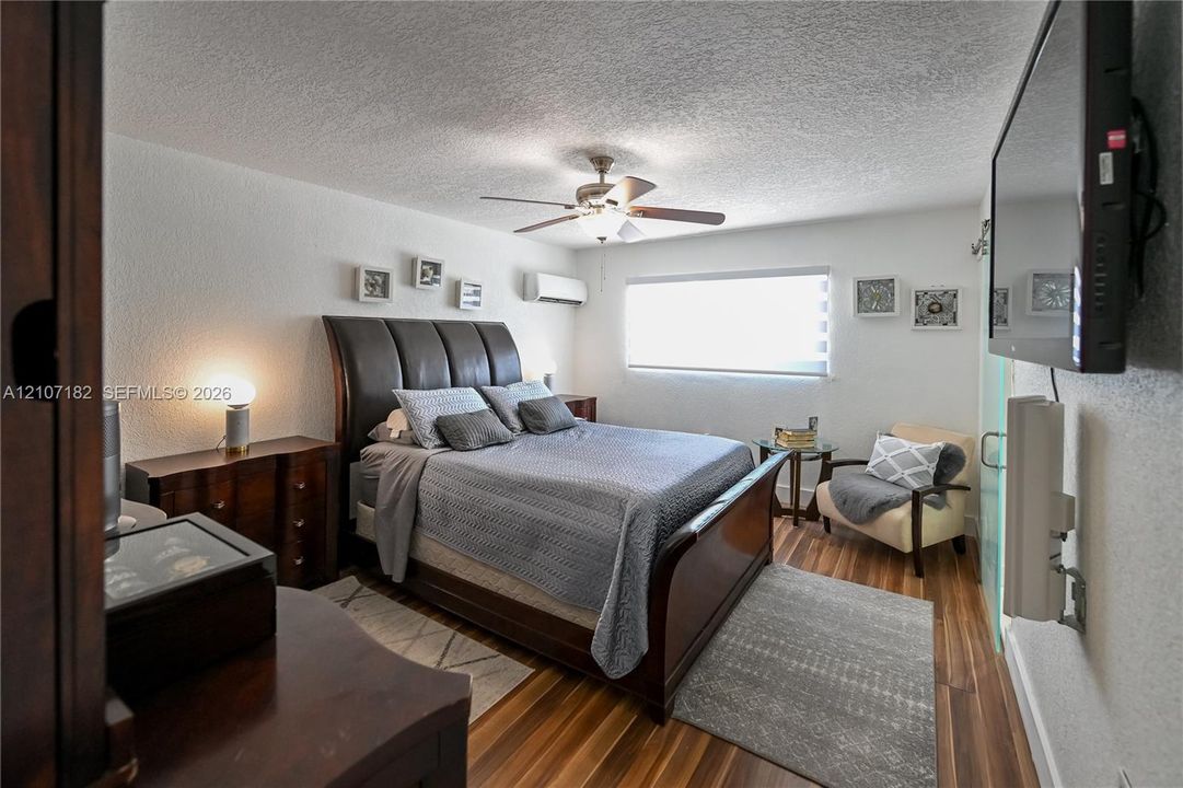 Room featuring wood-finish flooring, a wall-mounted ductless air conditioning unit, a ceiling fan with integrated lighting, and a window with horizontal blinds