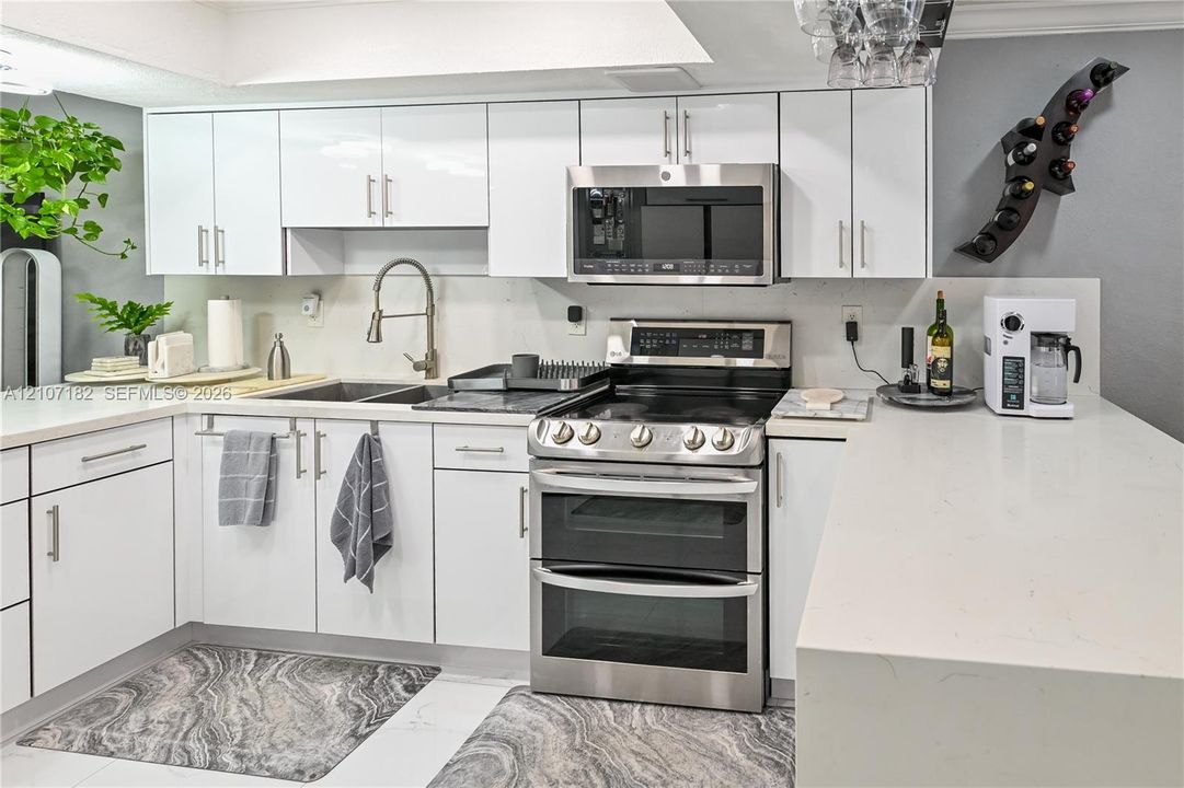 Kitchen featuring white slab-front cabinetry, light-toned quartz countertops, stainless steel dual-oven range, integrated microwave, and a high-arch gooseneck faucet
