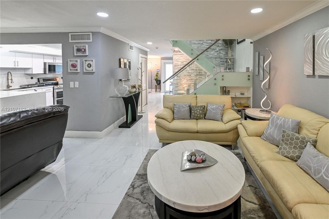 Open-concept area featuring white tile flooring, recessed lighting, and a staircase with glass panels and stone-veneer accent wall