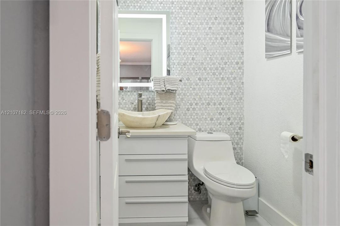 Bathroom featuring a white vanity cabinet with a stone vessel sink, polished metal faucet, integrated LED mirror, and geometric mosaic tile backsplash