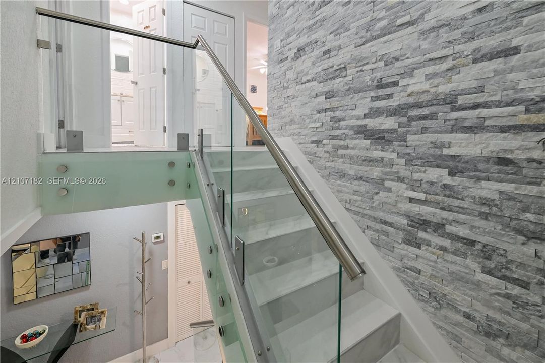 Staircase featuring stacked stone accent wall, glass panel railings, metal handrails, and solid-surface treads