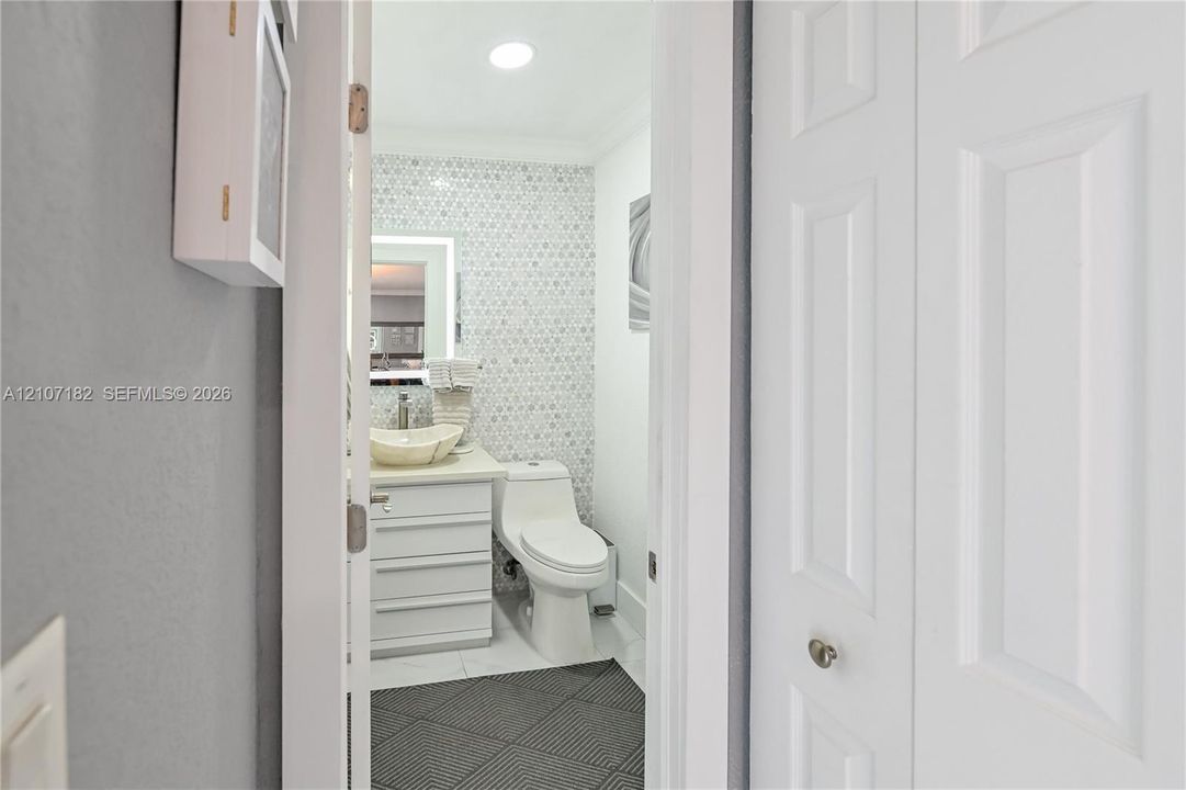 Bathroom featuring a white vanity cabinet with a vessel sink, geometric mosaic tile wall, one-piece dual-flush toilet, and diamond-patterned floor tile