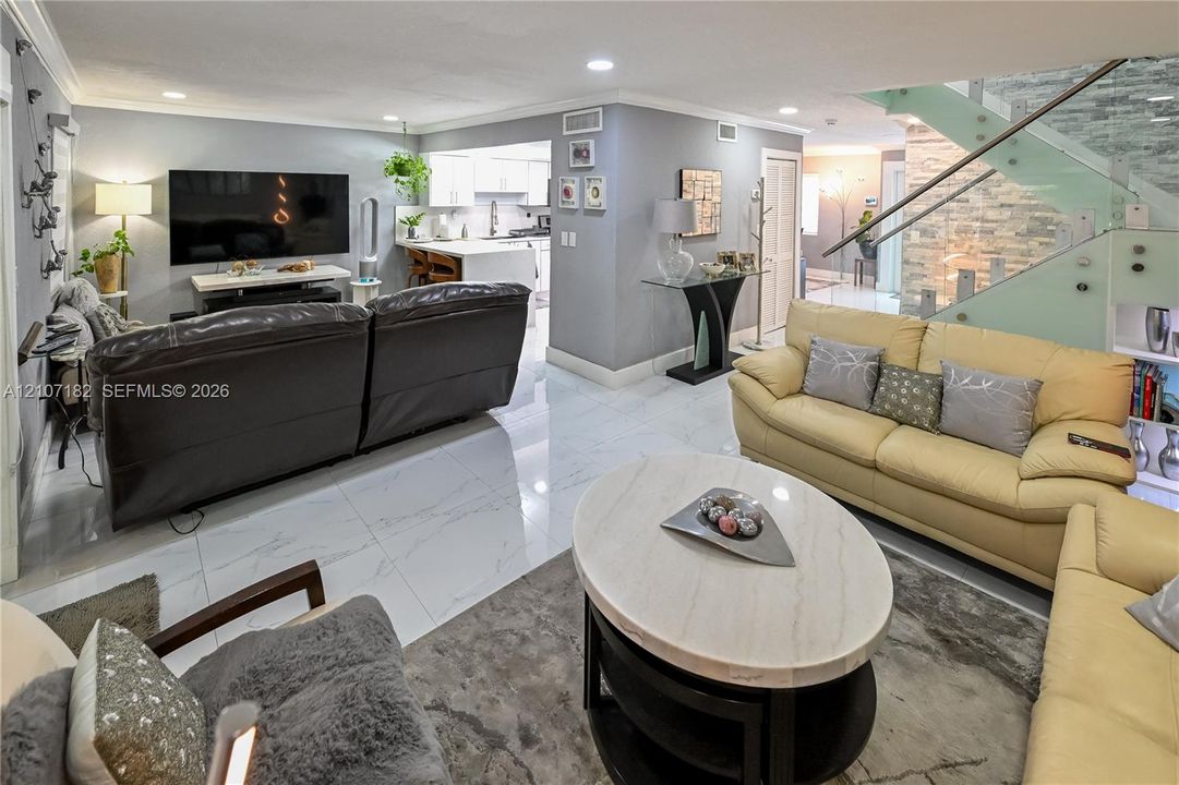 Large-format tile flooring, staircase with glass paneling and stainless steel railings, stone-accented wall, and recessed ceiling lighting