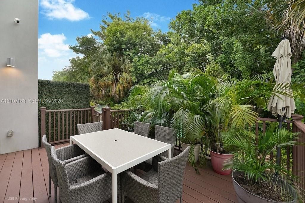 Elevated outdoor deck featuring composite wood-finish decking and a wooden balustrade, bordered by a privacy screen and mature perimeter vegetation