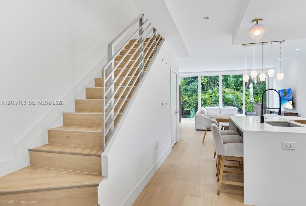 Staircase featuring wood-finish treads and metal horizontal railing, light wood-finish flooring, island with countertop and matte black faucet, and pendant lighting