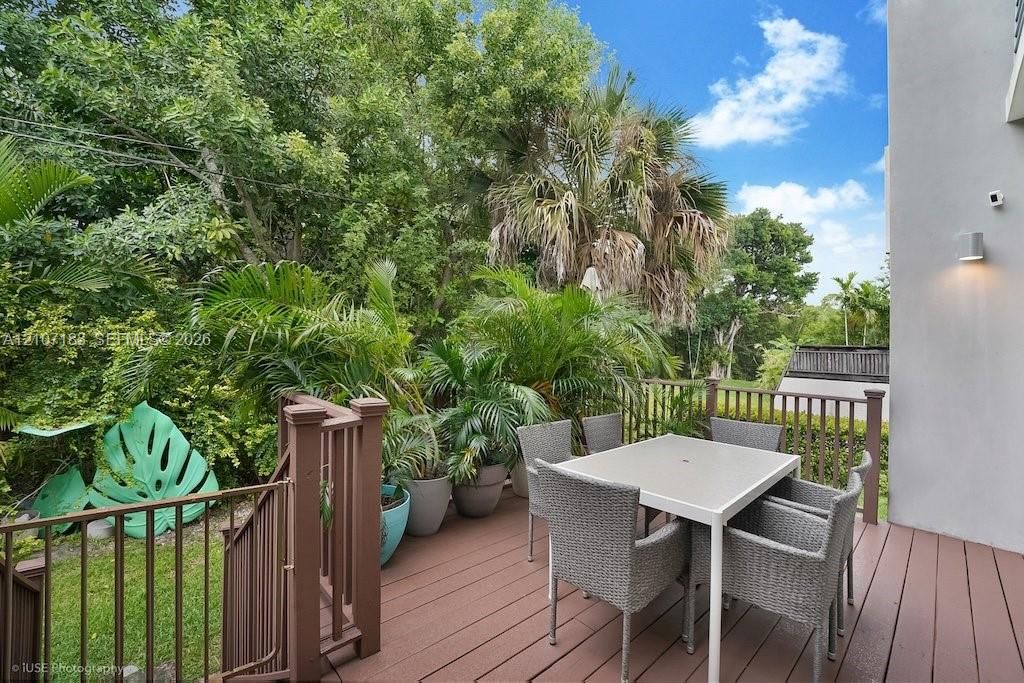 Elevated composite decking featuring custom railings, wall-mounted exterior lighting, and mature perimeter landscaping