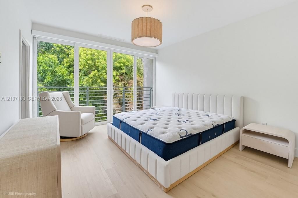Floor-to-ceiling glass sliding doors, wood-finish flooring, metal balcony railing, and a drum-style pendant light fixture