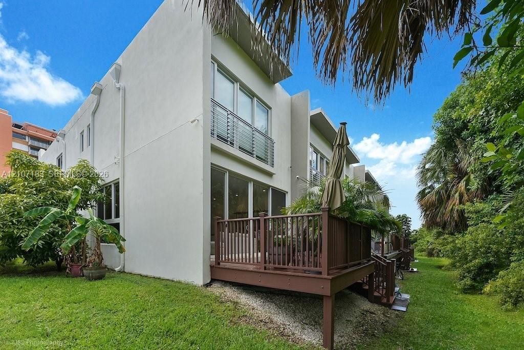 Modern two-story exterior featuring smooth stucco finish, elevated wooden deck, second-story balcony with metal railing, and extensive floor-to-ceiling glass sliding doors