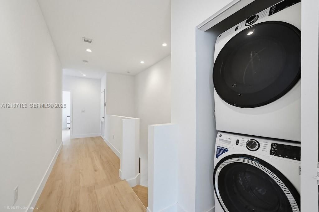 Stacked laundry appliance set featuring a front-load washer and dryer, wood-finish flooring, and recessed ceiling lighting