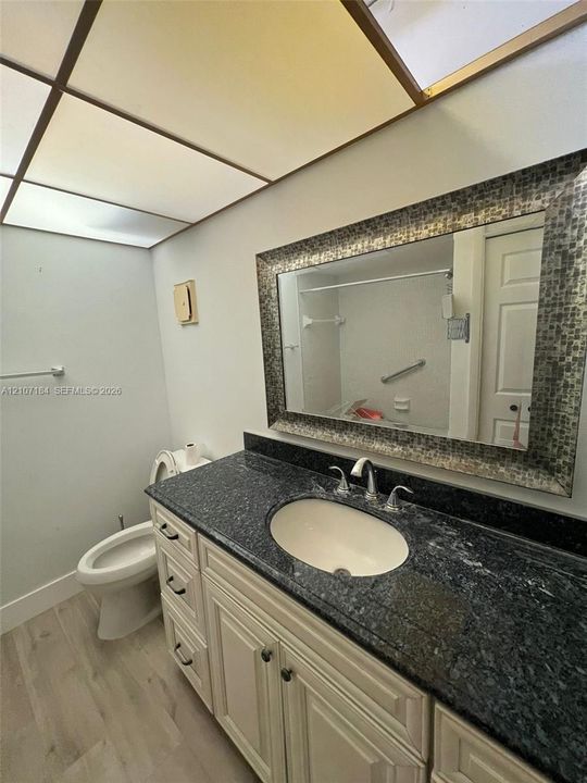 Bathroom featuring a stone vanity countertop with an integrated undermount sink, white cabinetry with dark hardware, a framed mosaic tile mirror, and recessed grid ceiling lighting