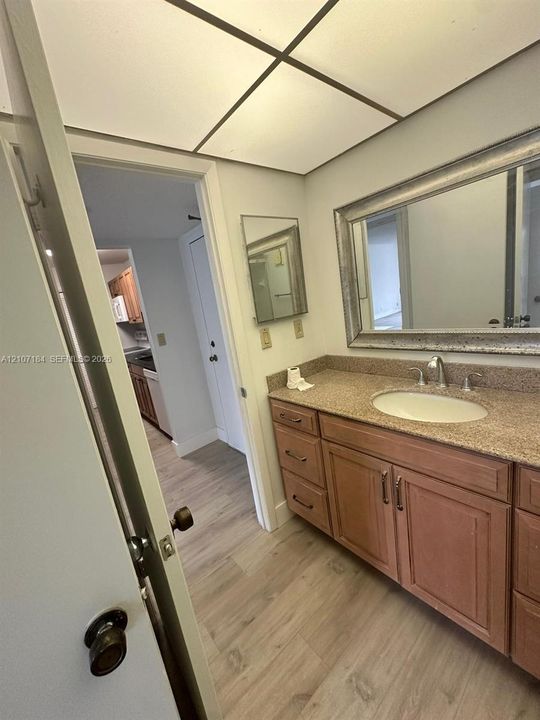 Bathroom vanity featuring wood cabinetry, stone-finish countertop with an integrated oval sink, and a wide-framed mirror, complemented by wood-finish flooring
