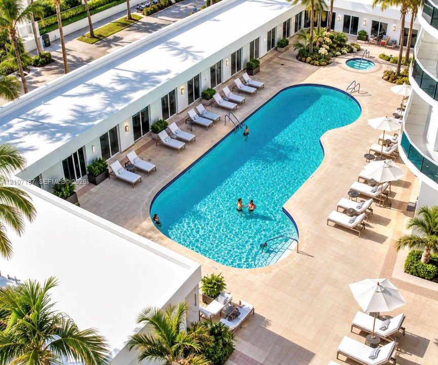 Courtyard pool area featuring a curved swimming pool, integrated spa, stone-paver decking, and manicured tropical landscaping