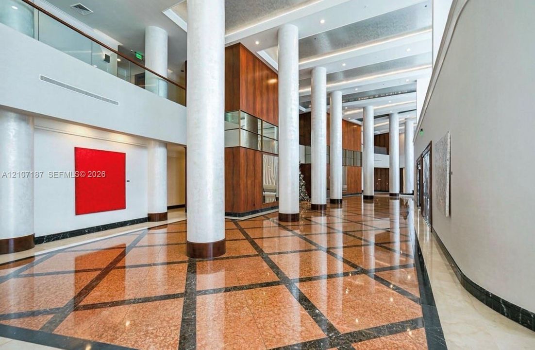 Grand atrium featuring soaring ceilings, polished stone tile flooring with geometric inlay, full-height decorative columns, and extensive wood-paneled wall accents
