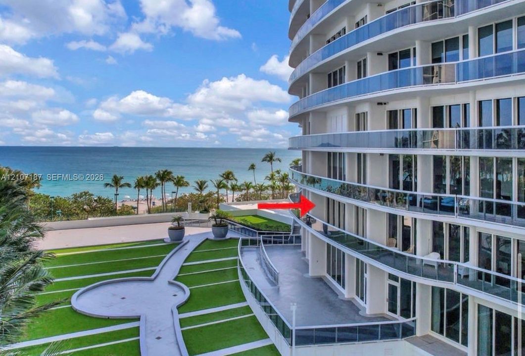 High-rise exterior featuring curved glass-railing balconies, floor-to-ceiling windows, and landscaped grounds with paved walking paths
