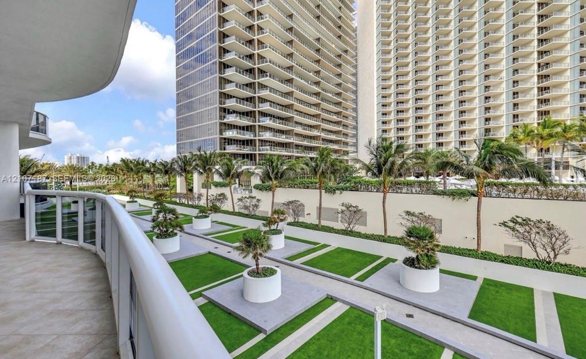 Private balcony featuring tile flooring, glass railing, and a geometric landscaped terrace with container plantings and paved pathways