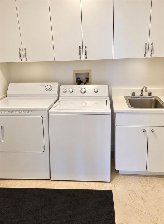 Laundry area featuring white cabinetry, a built-in utility sink with a stone-finish countertop, and tiled flooring